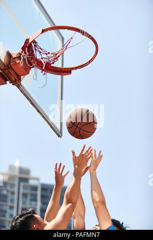young asian adults going up for rebounds on outdoor basketball court. Stock Photo