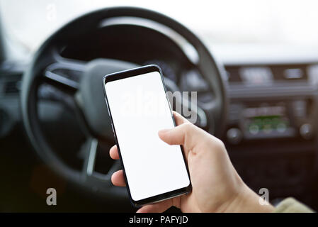 Close-up of man using smartphone in car on blurred dashboard background Stock Photo