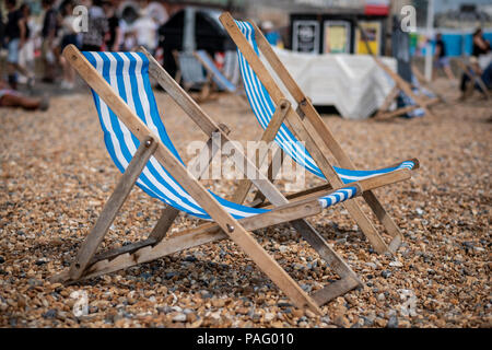 Two deckchairs sit on a pebble beach facing the sea in Brighton, UK Stock Photo