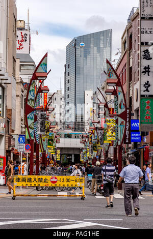 People walking into a crowded pedestrianised street in Tokyo, Japan with a new glass tower block in the background Stock Photo