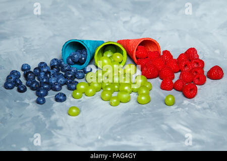 Juicy raspberries, blueberries and grapes in waffle cones on a gray background. Copy space. Stock Photo