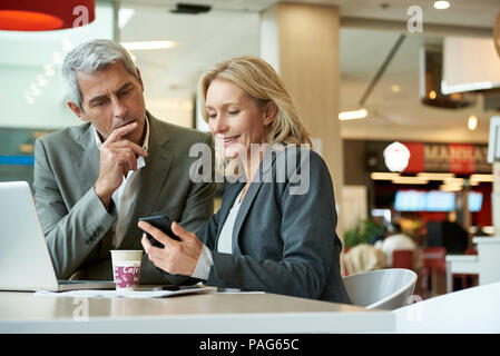 Businesspeople using smart phone in cafeteria Stock Photo