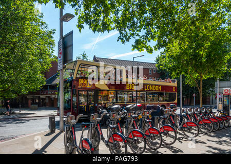 Transport for London's Santander cycles, self-hire bicycles, at Bermondsey docking station, Southwark. Open-topped sightseeing bus with tourists. Stock Photo