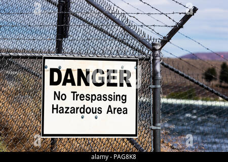 Dangerous no trespassing hazardous ares white sign on a barbed wire chain link fence with a river Stock Photo