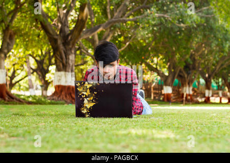 Young handsome student laying on grass and using laptop Stock Photo