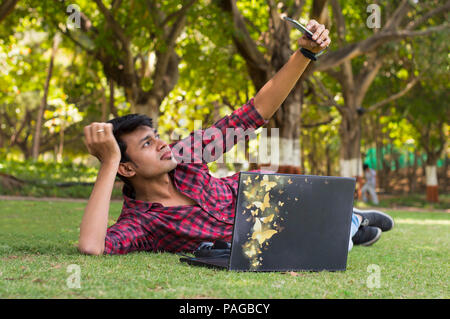 Young handsome student laying on grass and taking selfie with laptop Stock Photo