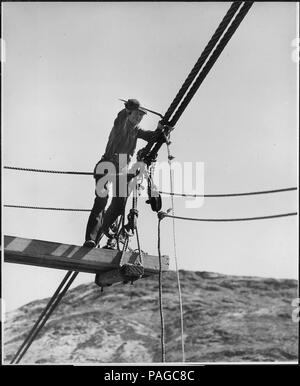 A rigger attaching suspenders to a pair of the 2-1-2 inch suspension cables of the sand and gravel conveyor bridge - Stock Photo