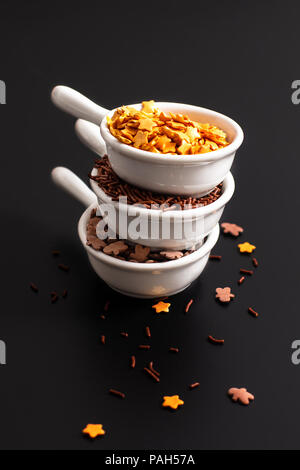 Food concept dessert decoration sugar spinkles chocolate and gold stars in white ceramic cups on black background Stock Photo