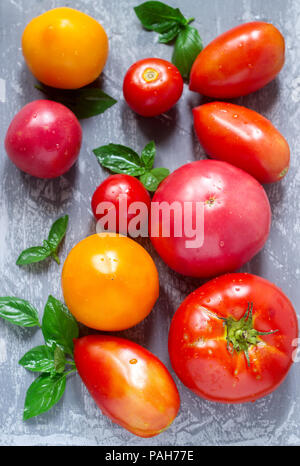 Different kinds of tomatoes and basil leaves on a concrete surface. Selective focus. Stock Photo
