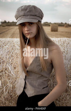 Girl with flat cap and waistcoat and straw in her mouth in a hay field Yorkshire Stock Photo