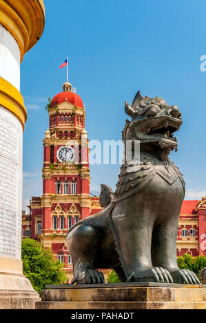 A half lion and half dragon stone sculpture at the foot of Independence Monument with High Court Building behind, Yangon, Myanmar Stock Photo