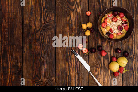 Breakfast with porridge, fruits and berries on weathered wooden textured table on background or old panels with cracks, scratches, swirls Stock Photo