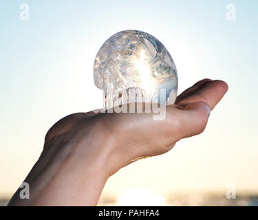 Woman's hand holding Clear Quartz Carved  Crystal Skull at the sunrise in front of the lake. Stock Photo