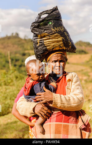 ANTANANARIVO, MADAGASCAR - JUNE 30, 2011: Unidentified Madagascar woman carries her child and some other things the street. People in Madagascar suffe Stock Photo