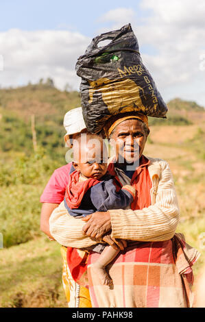 ANTANANARIVO, MADAGASCAR - JUNE 30, 2011: Unidentified Madagascar woman carries her child and some other things the street. People in Madagascar suffe Stock Photo
