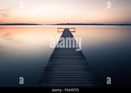 Old empty wooden jetty on lake, during sunrise. Stock Photo