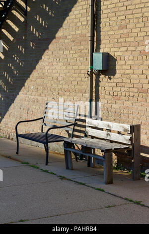 Industrial looking view of two park benches along a tan colored brick wall in an urban setting Stock Photo