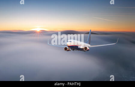 Passenger airplane. Landscape with big white airplane is flying in the red sky over the clouds and sea at colorful sunset. Passenger aircraft is landi Stock Photo