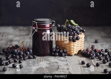 Aronia jam next to fresh berries. Homemade aronia jam in glass jar with fresh aronia berries on wooden table. Stock Photo