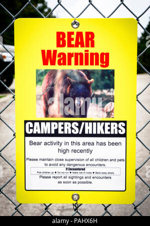 A bear warning sign hangs on a cyclone fence as an advisory to campers and hikers of high bear activity in area Stock Photo