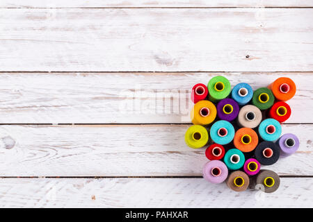 Beautiful sewing spools with bright vivid threads placed on white rough wooden plank table from above Stock Photo