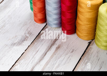 Close-up background of colorful vibrant silk threads on sewing spools on white wooden table Stock Photo