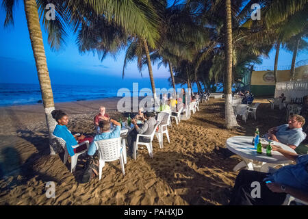 Groups of people are seated at tables along the beach at a restaurant. Monrovia, Liberia Stock Photo