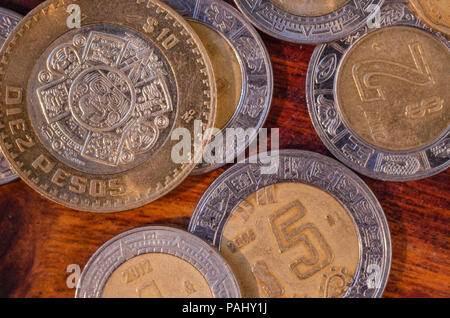 Mexican Coins of $5 and $10 pesos in the middle of other coins in a table of wood suggesting good economy Stock Photo