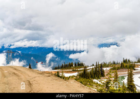 View from a country road to thick, low clouds in the mountains, covered with trees and snow above the ski resort with the gondola of the cable car and Stock Photo