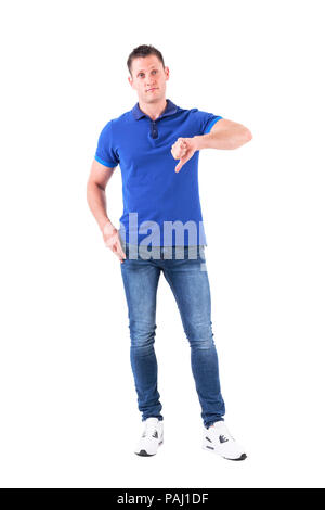 Unsure confused adult man in blue polo shirt showing thumbs down and looking up doubtfully. Full body isolated on white background. Stock Photo