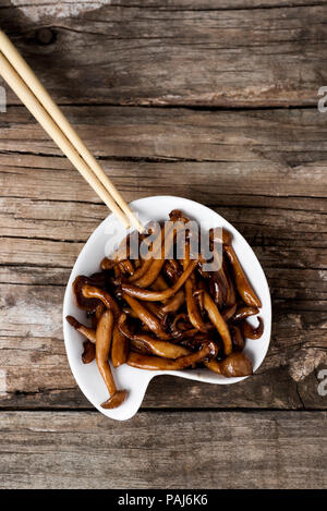 high angle view of a white ceramic bowl with sauteed japanese bunapi-shimeji mushrooms, also known as white beech or white clamshell mushrooms, on a r Stock Photo