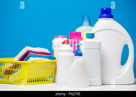 Photo of several bottles of cleaning products and multi-colored towels in basket isolated on blue background Stock Photo