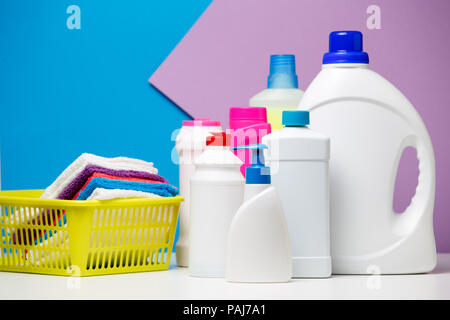 Photo of several bottles of cleaning products and multi-colored towels in basket isolated on violet,blue background Stock Photo