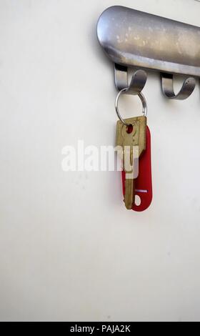 Red plastic key ring and key hanging on wall hook Stock Photo