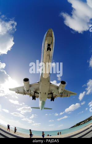 people watching the B757 on final-approach landing low over the sea at Maho Beach with a few clouds Stock Photo