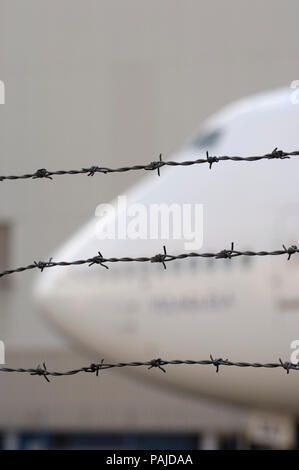 barbed-wire airport perimeter fence with windshield and upper and lower deck windows of a South African Airways Boeing 747-400 behind Stock Photo