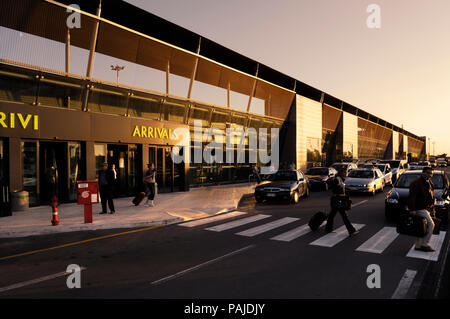 passengers with bags walking and private cars on the road outside the terminal Stock Photo