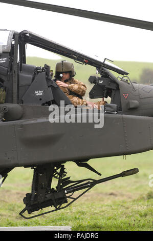 pilot wearing helmet in the cockpit of a British Army Air Corps Boeing WAH-64D Apache AH-1 with 30 millimetre chain-gun parked on the grass at the Bri Stock Photo
