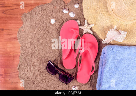 Top view of summer background with flip flops, hat, towel, glasses and shells on sand and wooden plank with space for sample text Stock Photo