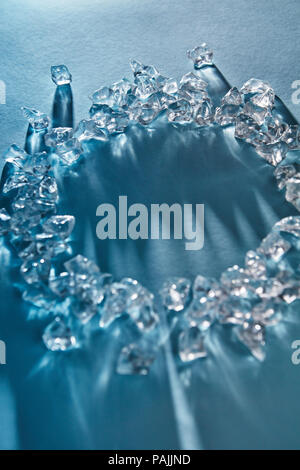 Long shadows and reflections from transparent pieces of crushed ice cubes in the round form on a blue background with soft focus. Stock Photo