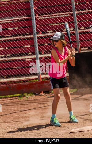 Eight yeqr old girl, in red  tank top, sun glassees, shorts and hat, getting ready to swing bat. Model Relese $104 Stock Photo