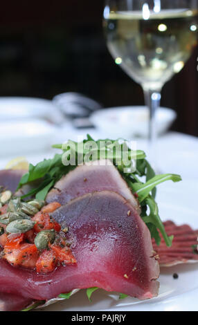 Slices of bluefin tuna served in restaurant with pumpkin seeds, tomato, raw rocket and white wine - macro side view Stock Photo
