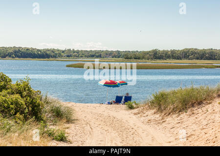 a couple sitting under beach umbrellas at a bay beach in East Hampton, NY Stock Photo
