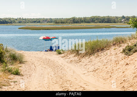 a couple sitting under beach umbrellas at a bay beach in East Hampton, NY Stock Photo
