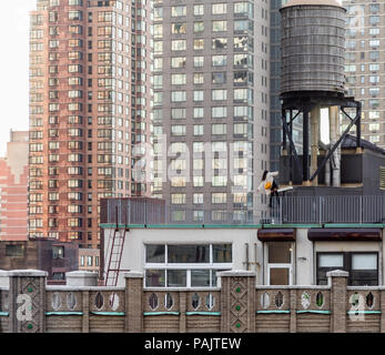 well dressed young woman climbing the ladder of a water tower on the roof of a NYC building Stock Photo