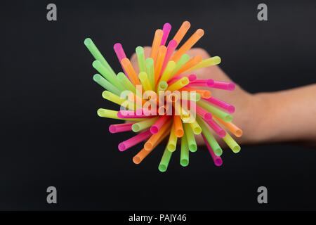 Swirl of bright colorful drink straws bunch in hand as plastic single use disposable harmful ecological issue concept isolated on black background Stock Photo