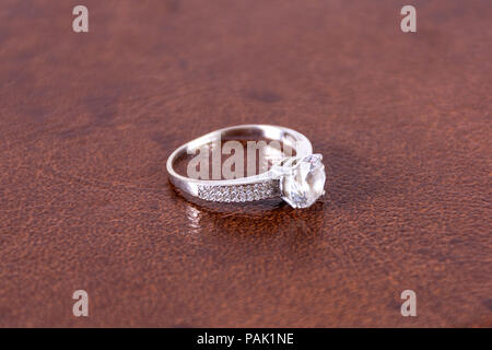 Diamond silver engagement wedding ring on leather brown blurred and soft background in studio. Love and married concept. Close up, selective focus Stock Photo