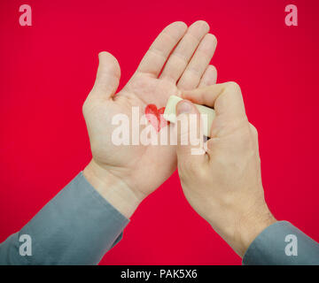 Deleting memories of a love romantic relationship or forgeting someone dear like an ex partener suggested by a man erasing a heart from his palm on a  Stock Photo
