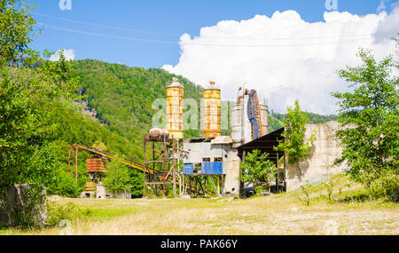 Old abandoned industrial exploatation site factory with towers and reservoirs rusting in a desserted area with green wood and a blue sky Stock Photo
