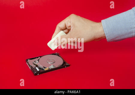 Deleting erasing and hiding all information from a hard drive and from the world suggesting by a business man hand erasing a hard disk on a red alerte Stock Photo